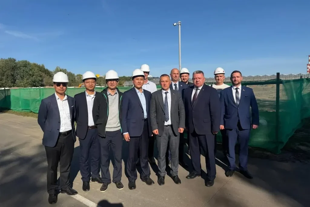 Delegation in hard hats beside a fenced greenhouse construction site