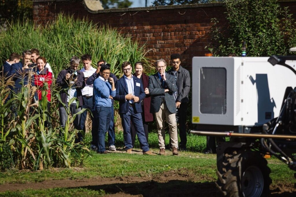 Visitors observing an agricultural research robot beside crop plots