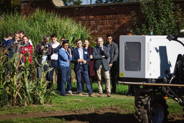 Visitors observing an agricultural research robot beside crop plots